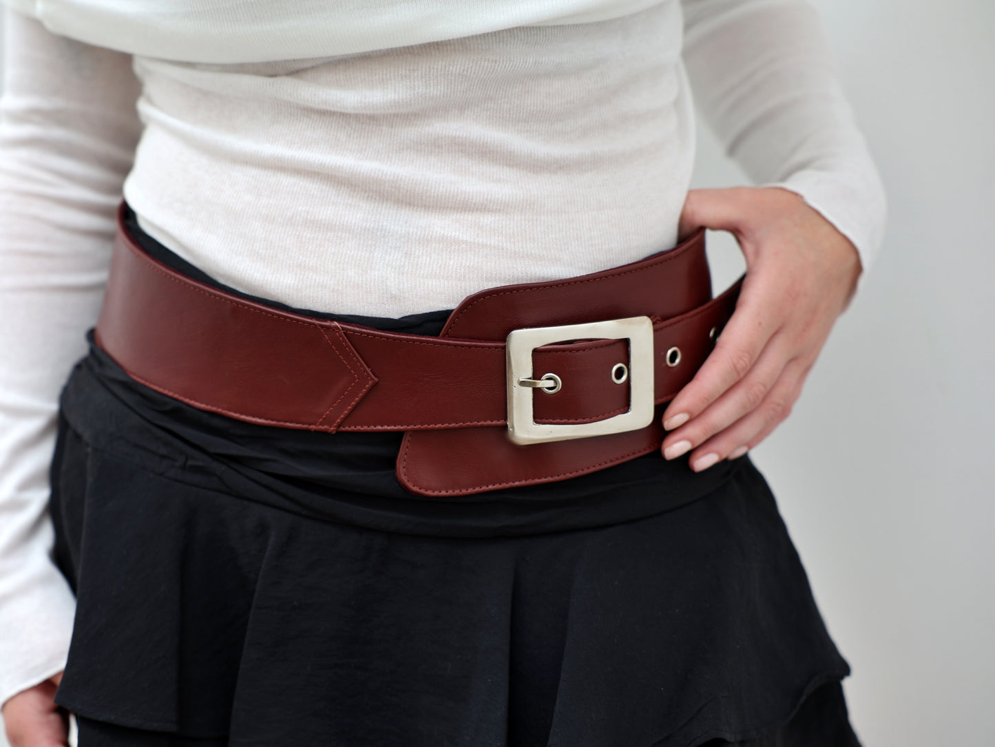 Person wearing a brown belt with a white shirt and black skirt on a light gray background